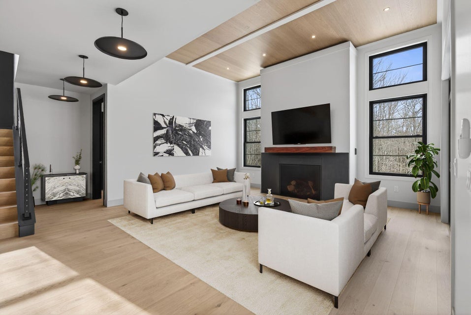 Contemporary custom living room featuring a tall fireplace wall, mounted television, wood-paneled ceiling, black-framed windows, and white sofas arranged around a coffee table.