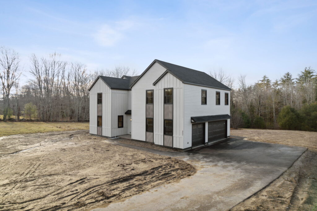 Newly constructed two-story white home with black-framed windows, a dark roof, attached two-car garage, and paved driveway on a spacious Maine property.