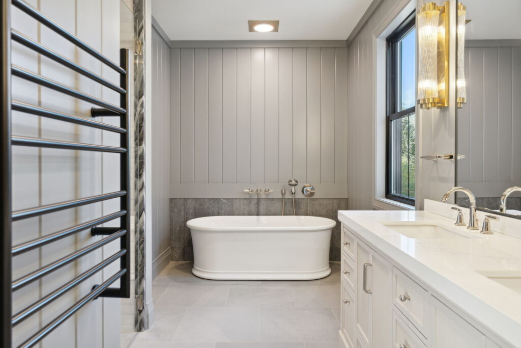 Custom primary bathroom featuring a freestanding soaking tub, gray vertical shiplap walls, natural light, and a spacious vanity.