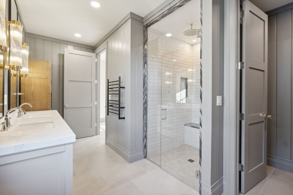 Custom bathroom with a glass-enclosed walk-in shower, white subway tile, marble trim, gray paneled walls, and a heated towel rack.